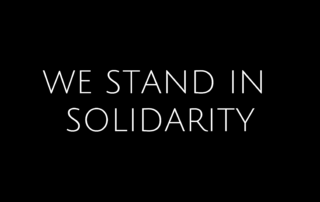 White Text "We Stand In Solidarity" on a black background